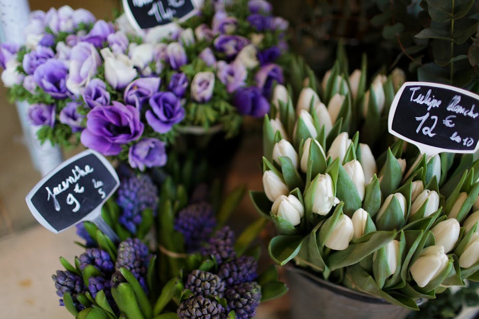 A close-up view of a floral display featuring fresh purple and white flowers, including a bouquet of purple lisianthus with delicate, ruffled petals and white tulips with smooth, closed petals, arrang